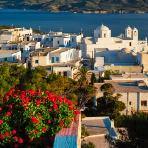 Picturesque scenic view of Greek town Plaka on Milos island over red geranium flowers and Orthodox greek church. Plaka village, Milos island, Greece